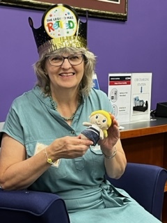 Nancy sitting in a chair holding a doll with yellow hair and wearing a retired crown.